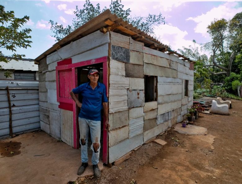 Un hombre posa afuera de su casa durante un corte de energía eléctrica. A la izquierda, en medio de la oscuridad de su casa, Catalina, de 35 años, repasa los problemas de su día a día