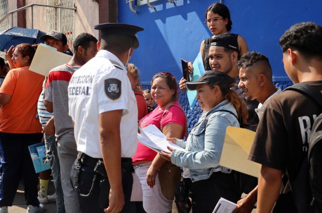 Agentes hablan con migrantes que hacen fila en espera de resolver su situación migratoria en Tapachula