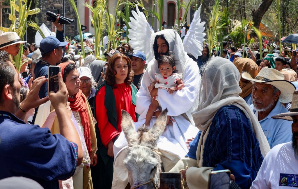 El joven que personifica a Jesús de Nazaret en la representación del Domingo de Ramos en la alcaldía de Iztapalapa, en Ciudad de México, subió a algunos niños al burrito. La jornada transcurrió con calma