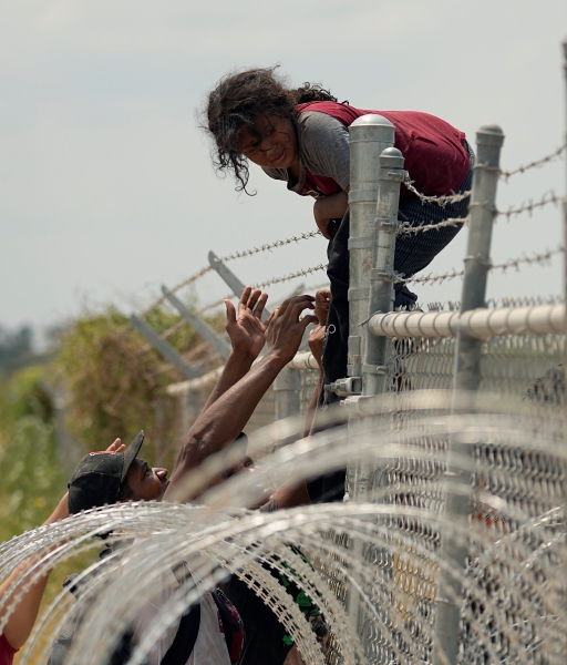 Migrantes cruzan una cerca en la frontera entre México y Estados Unidos, en Tijuana