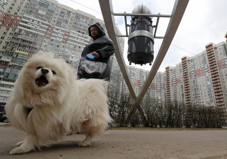 Un vendedor de fresas habla con un cliente frente a un mural que representa a un cosmonauta en el bulevar de los Cosmonautas en Krasnogorsk, a las afueras de Moscú. A la izquierda, una mujer pasea a su perro frente a un modelo de nave espacial rusa en la misma zona