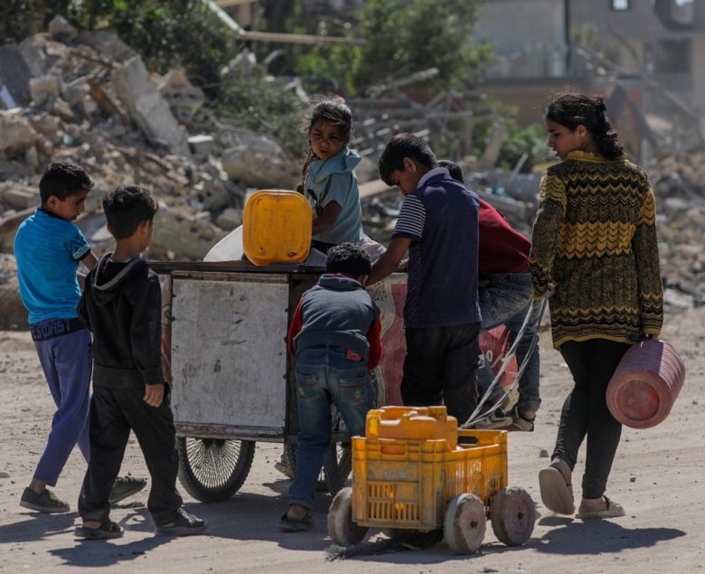 Un grupo de niños palestinos desplazados internos camina para llenar botes de agua después de regresar a la ciudad de Khan Younis, en el sur de la Franja de Gaza