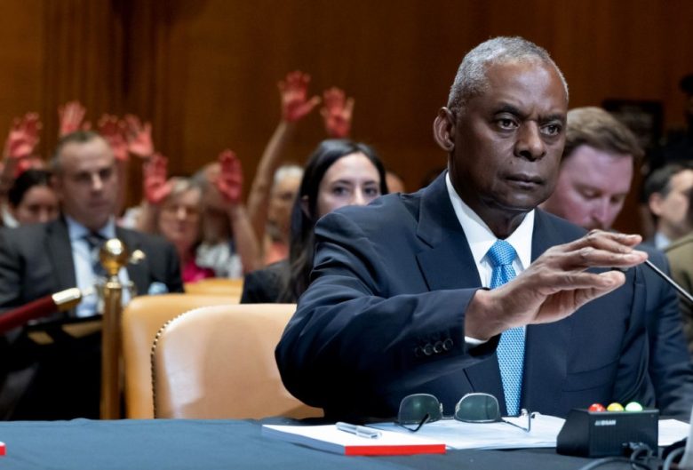 Manifestantes propalestinos (atrás) levantan las manos mientras el secretario de Defensa de los Estados Unidos, Lloyd Austin, comparece ante una audiencia del subcomité de Asignaciones del Senado. A la izquierda, niños oyen un discurso en una marcha proisraelí en los Ángeles, California