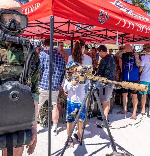 Un pequeño manipula un dispositivo de artillería remoto en la “aldea del ejército” durante las celebraciones del fin de semana del Día de los Caídos en Miami Beach. A la izquierda, otro niño un observa a través de la mirilla telescópica de un rifle de francotirador en el área de equipo militar que instaló el Ejército estadonunidense en la playa de Miami