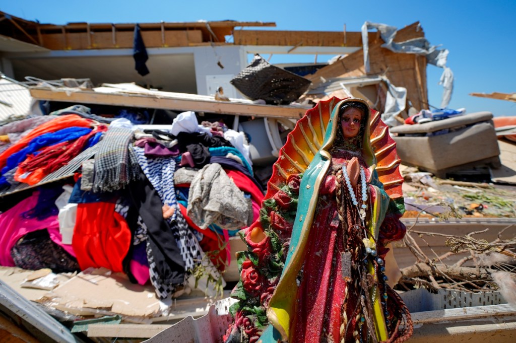 Una figura de la Virgen de Guadalupe entre los escombros de la casa destruida de Juana Landeros, quien sobrevivió a un tornado mortal con su esposo y su hijo de 9 años el domingo en la noche, en Valley View, Texas. A la derecha, dos jóvenes retiran escombros de un comercio en Arkansas