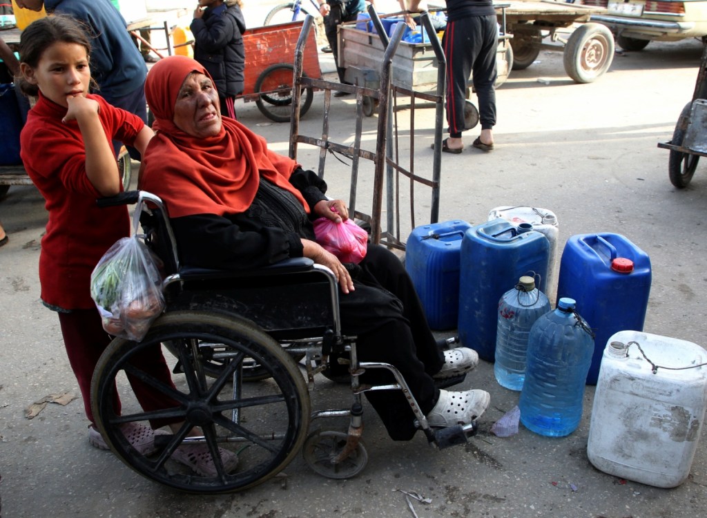 Sobre estas líneas, niños palestinos reciben ayuda humanitaria en la ciudad de Rafah, en una zona castigada por ataques aéreos israelíes. A la izquierda, personas esperan para obtener agua