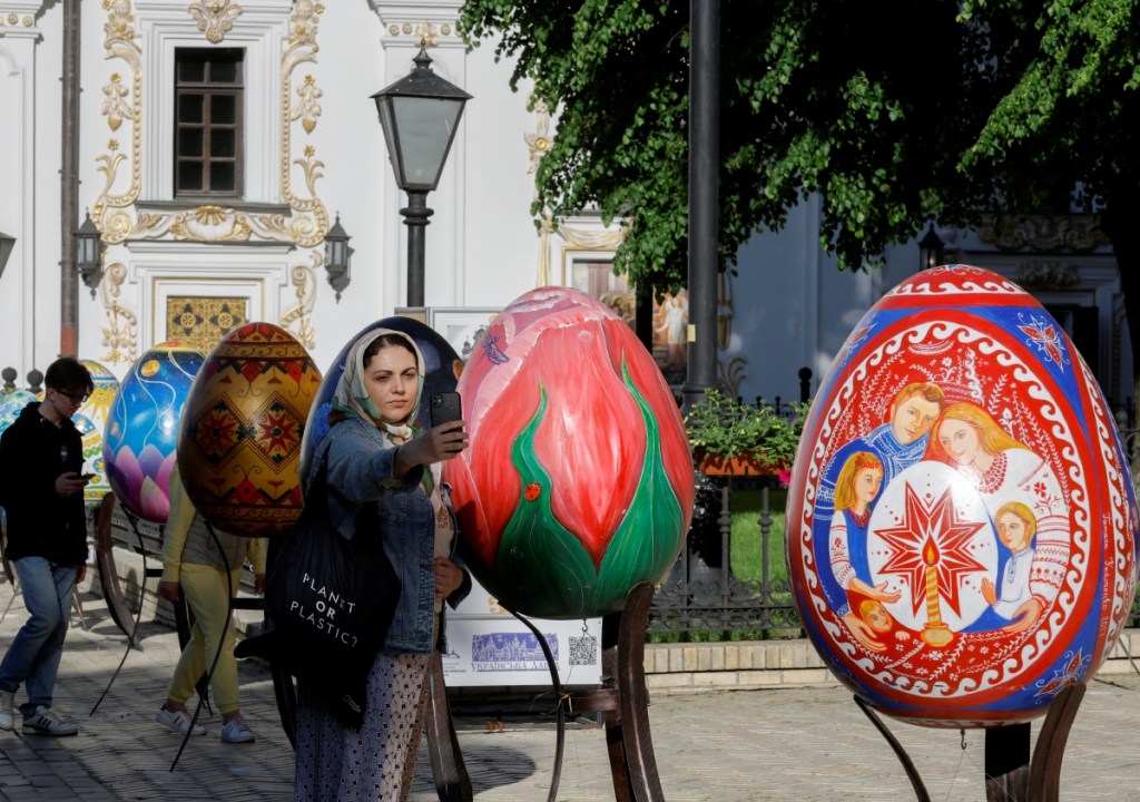 El patriarca ecuménico Bartolomé I, líder espiritual del mundo ortodoxo griego, oficia la ceremonia en la Iglesia de San Jorge en Estambul. A la izquierda, una mujer se toma un selfie con huevos de pascua en Kiev, Ucrania