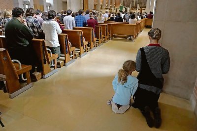 Una mujer y una niña rezan de rodillas durante una misa católica en el Benedictine College, el 29 de octubre de 2023, en la ciudad de Atchison, Kansas, en los EE.UU.