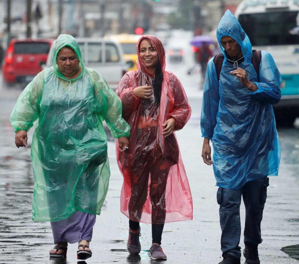 Un miembro de protección civil inspecciona el caudal de un río en San Salvador, El Salvador. A la izquierda, tres personas se protegen de la lluvia. La Dirección General de Protección Civil declaró alerta roja en todo el país por las fuertes lluvias registradas en las últimas horas y por las altas probabilidades de inundaciones urbanas y desbordamiento de ríos