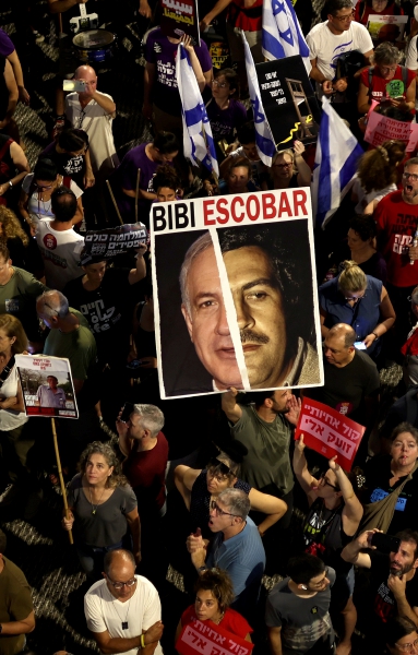 Manifestantes portan una pancarta que representa al primer ministro israelí, Benjamín Netanyahu, como Pablo Escobar, durante una protesta, ayer en Tel Aviv