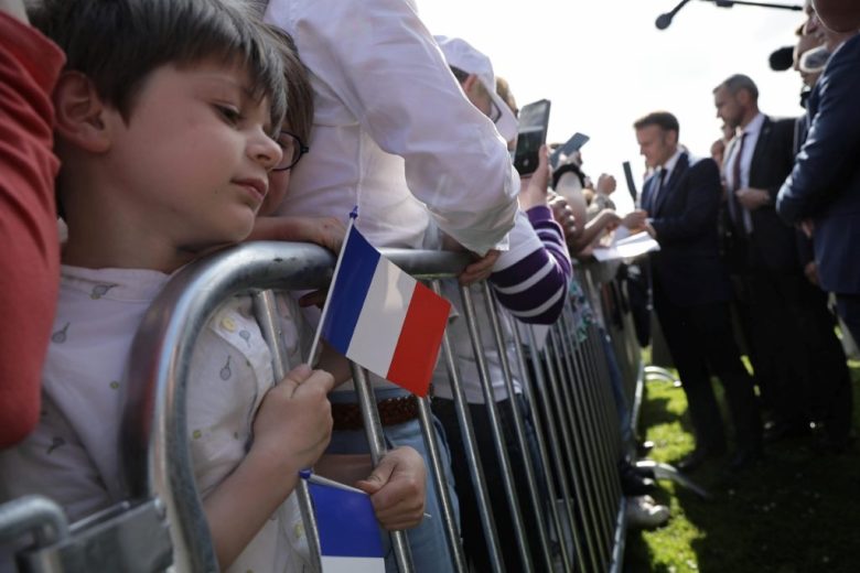 Un niño sostiene banderitas francesas durante la ceremonia encabezada por el presidente francés, Emmanuel Macron (centro), quien saluda a los asistentes en la ciudad de Saint-Lo. A la derecha, Achille Muller, el último superviviente de las Fuerzas Francesas Libres, ayer
