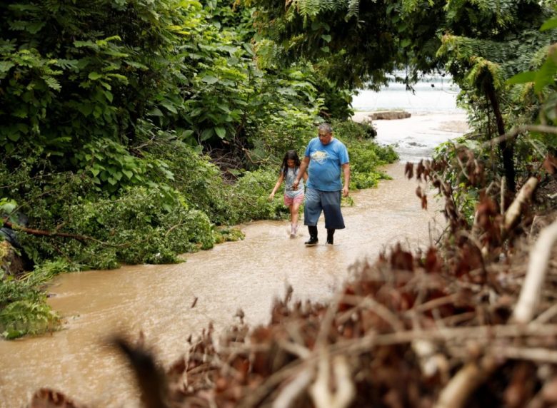 Arriba, un hombre observa los escombros de una casa afectada por un derrumbe en la madrugada de ayer viernes, en Soyapango, El Salvador. A la izquierda, un hombre y una niña caminan por un sendero inundado por el desbordamiento de un río debido a las lluvias en el país, en Santiago Texacuangos
