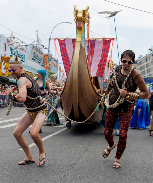 Integrantes de una comparsa tiran de una carroza en el desfile anual de Coney Island. A la derecha, una asistente con colorido disfraz de sirena