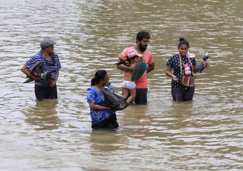 Un hombre empuja a dos niños en una balsa improvisada en una calle inundada por fuertes lluvias en un suburbio de Colombo, Sri Lanka. A la izquierda, otra familia de damnificados