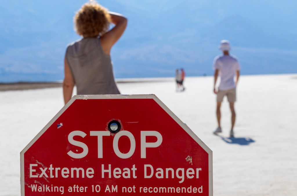 Visitantes en el Parque Nacional Death Valley, California, junto a un letrero que advierte del calor extremo