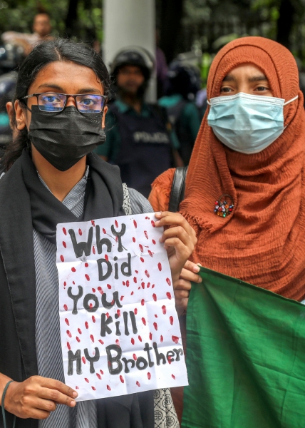 Manifestantes gritan consignas mientras participan en la “Marcha por la Justicia”, frente al área de la Corte Suprema en Daca, Bangladesh. A la derecha, guardias fronterizos de Bangladesh hacen guardia en la manifestación