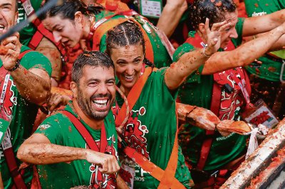 Vista aérea de Buñol, participantes VIP en un camión de tomates, la multitud bañada de rojo y una joven prueba su puntería con dos combatientes que la desafían