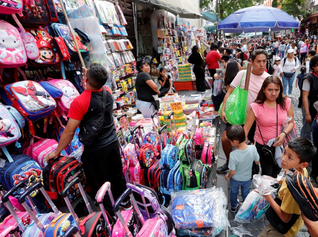 Pequeños que hoy regresan a las aulas observan a las mochilas que, como se puede ver a la izquierda, acomodan los comerciantes que tuvieron un movido cierre vacacional en los distintos puntos de venta en Ciudad de México y alrededores