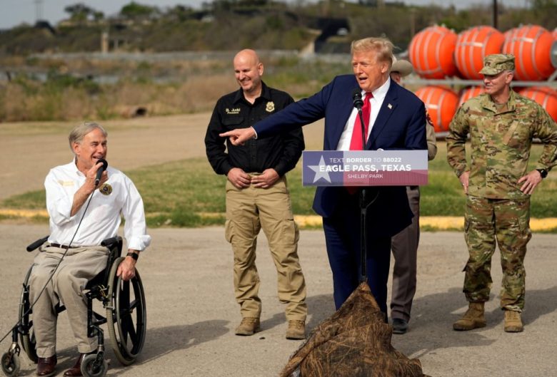 El expresidente Donald Trump señala al gobernador de Texas, Greg Abbott, mientras pronuncia un discurso en el parque Shelby durante una visita a la frontera con México, el jueves 29 de febrero de 2024, en Eagle Pass. Trump y Abbott coinciden en sus posturas sobre la migración ilegal. A la izquierda, agentes de la Patrulla Fronteriza de EE.UU. detienen a varios hombres sospechosos de haber cruzado ilegalmente a Texas