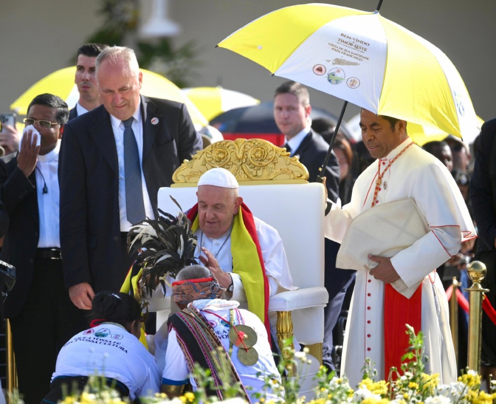 El papa Francisco bendice a los fieles durante una misa en la explanada de Taci Tolu, en Dili, Timor Oriental. A la derecha, un asistente sostiene figuras religiosas durante una misa oficiada por el Papa