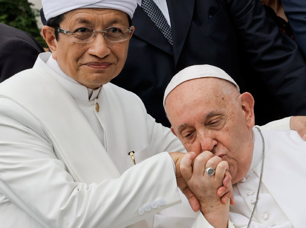 El papa Francisco besa la mano del gran imán de la mezquita Istiqlal, Nasaruddin Umar, tras un encuentro con líderes religiosos en Yakarta. A la derecha, escenario preparado para la santa misa