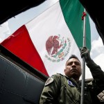 Un miembro de la Fuerza Aérea Mexicana sostiene la bandera en una de las naves que participaron en el desfile conmemorativo del 214 aniversario de la Independencia