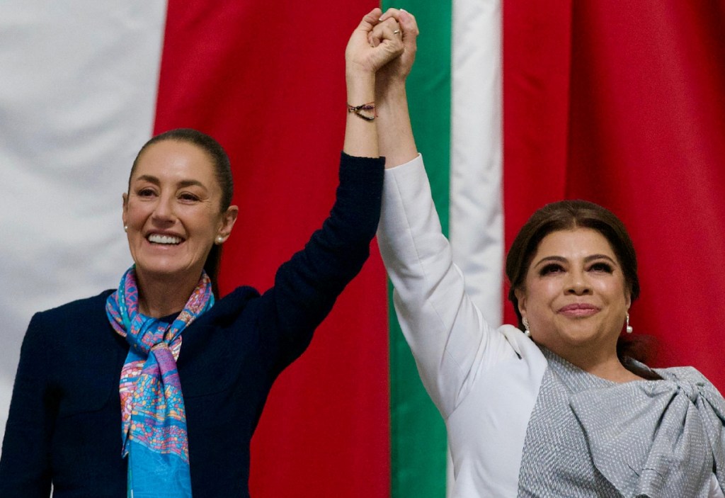 La presidenta Claudia Sheinbaum —izquierda— levanta la mano a Clara Brugada, la nueva jefa de gobierno de Ciudad de México, ayer