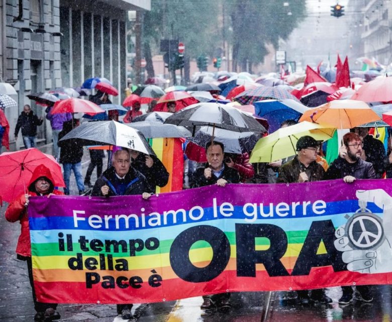 Manifestantes de Turín caminan con una manta que dice “Paremos la guerra. El momento de la paz es ahora”. A la derecha, una pareja de participantes en la caminata de Turín se protege con impermeables de la lluvia que cayó ayer en la ciudad durante las protestas masivas en Italia