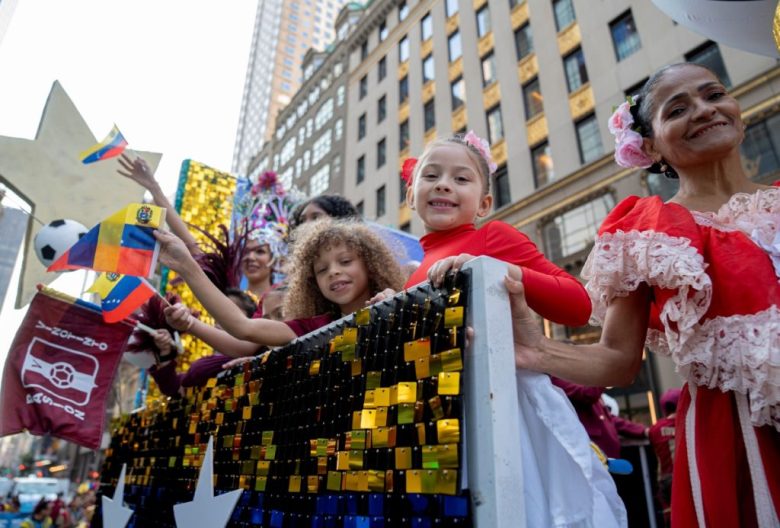 Dos mujeres con los colores de la bandera puertorriqueña durante el desfile por el Día de la Hispanidad, ayer en Nueva York. A la derecha, personas que asistieron al desfile portan banderas de España y gritan vítores al paso de la columna