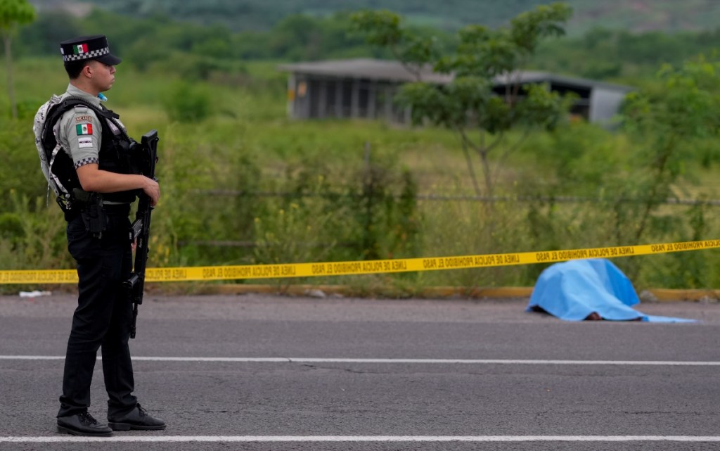 Un oficial de la Guardia Nacional vigila un tramo carretero acordonado, con el cadáver de una persona de fondo, tras un hecho violento