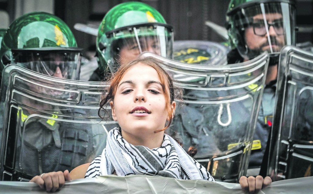 Una joven manifestante se coloca adelante de un cerco de la policía antidisturbios que custodia el céntrico Palacio Real de Nápoles, sede de la Reunión de Ministros del G7 sobre Defensa, que se inició ayer