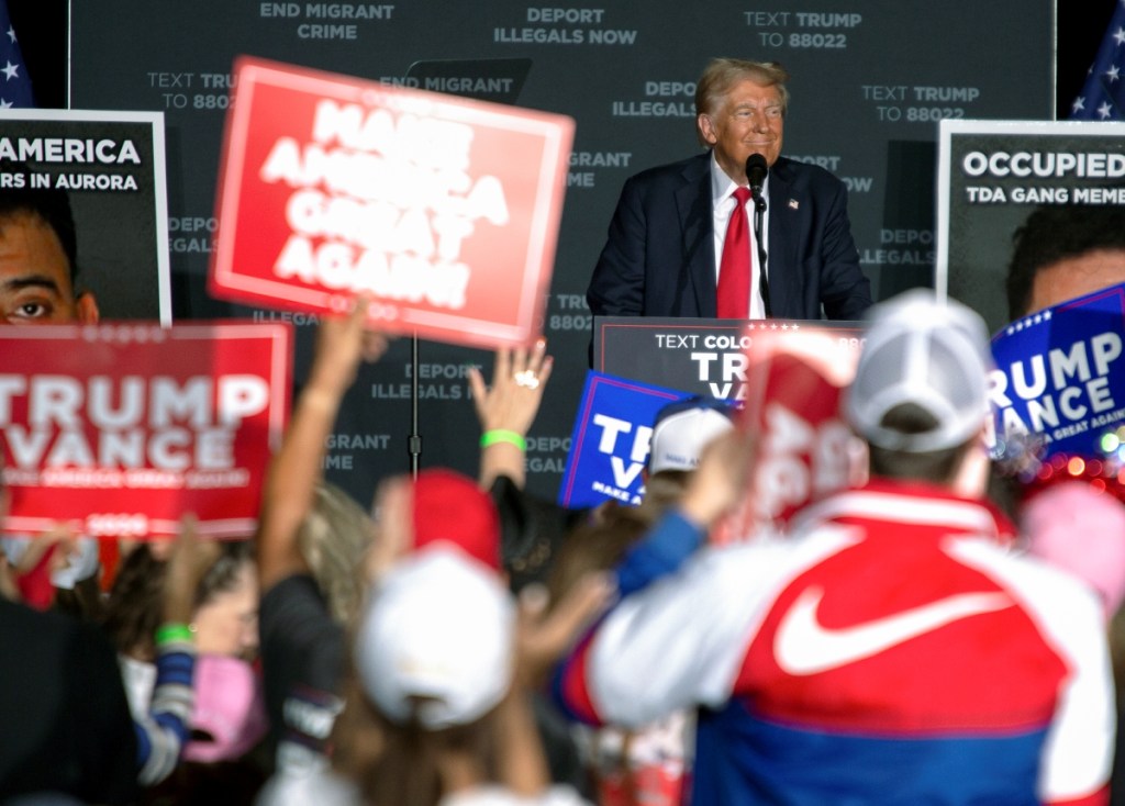 Donald Trump habla durante un mitin en Gaylord Rockies and Resort en Aurora, Colorado. A la izquierda, un simpatizante del Trump muestra unos anillos con el rostro de aquél en el acto de campaña en la misma ciudad