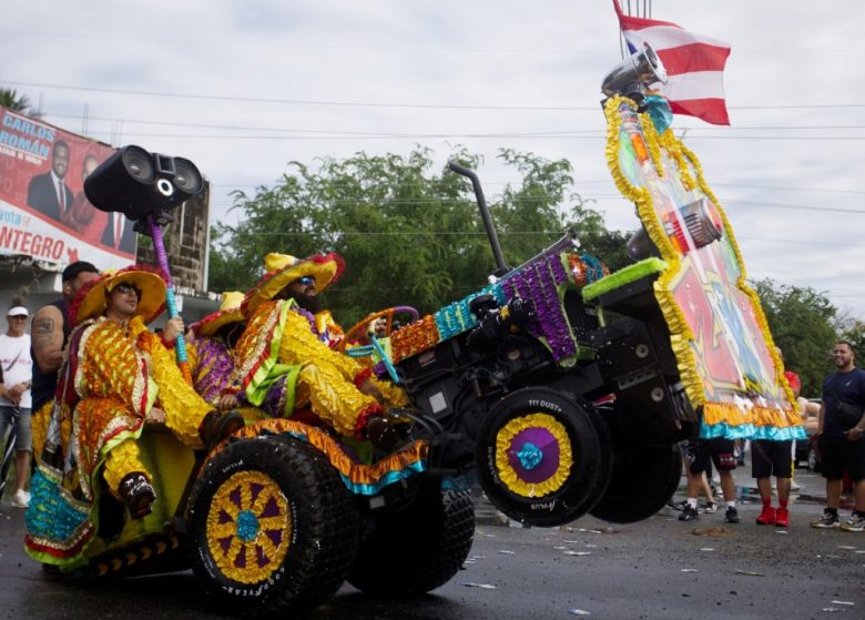 Una persona disfrazada participa en el Festival de las Máscaras de Hatillo, Puerto Rico. A la izquierda, un vehículo forrado con papel de colores para la festividad que se lleva al cabo formalmente desde 1970 y que, con el paso del tiempo, ha ganado adeptos entre los puertorriqueños