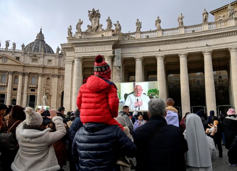 Visitantes observan al papa Francisco en una pantalla gigante