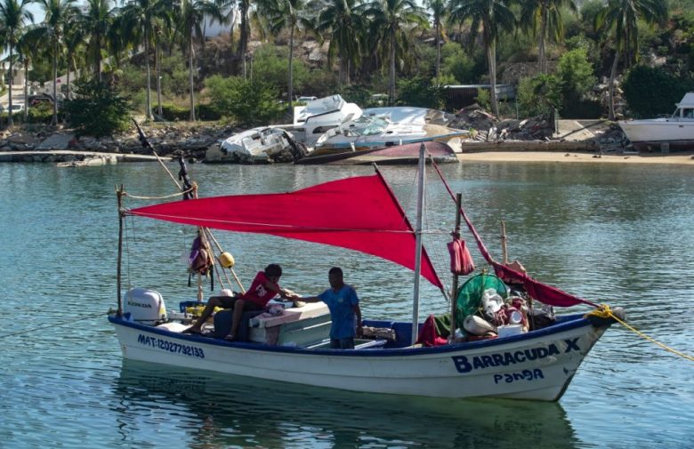 Las dos caras de la moneda: un barco pesquero navega por la costa de Acapulco, mientras en tierra se encuentran restos de embarcaciones afectadas por “Otis”. A la izquierda se observa una muestra de ello