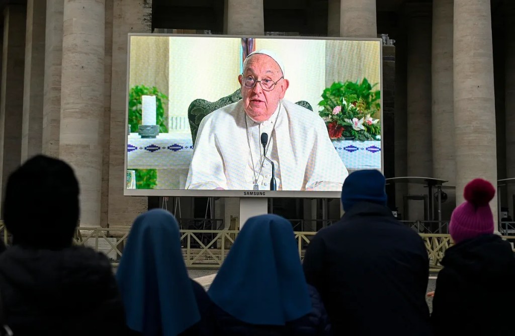 Fieles se reúnen ante una pantalla que muestra al papa Francisco presidir el rezo del Ángelus dominical, donde llamó a un alto a las guerras en Navidad (Foto de EFE)