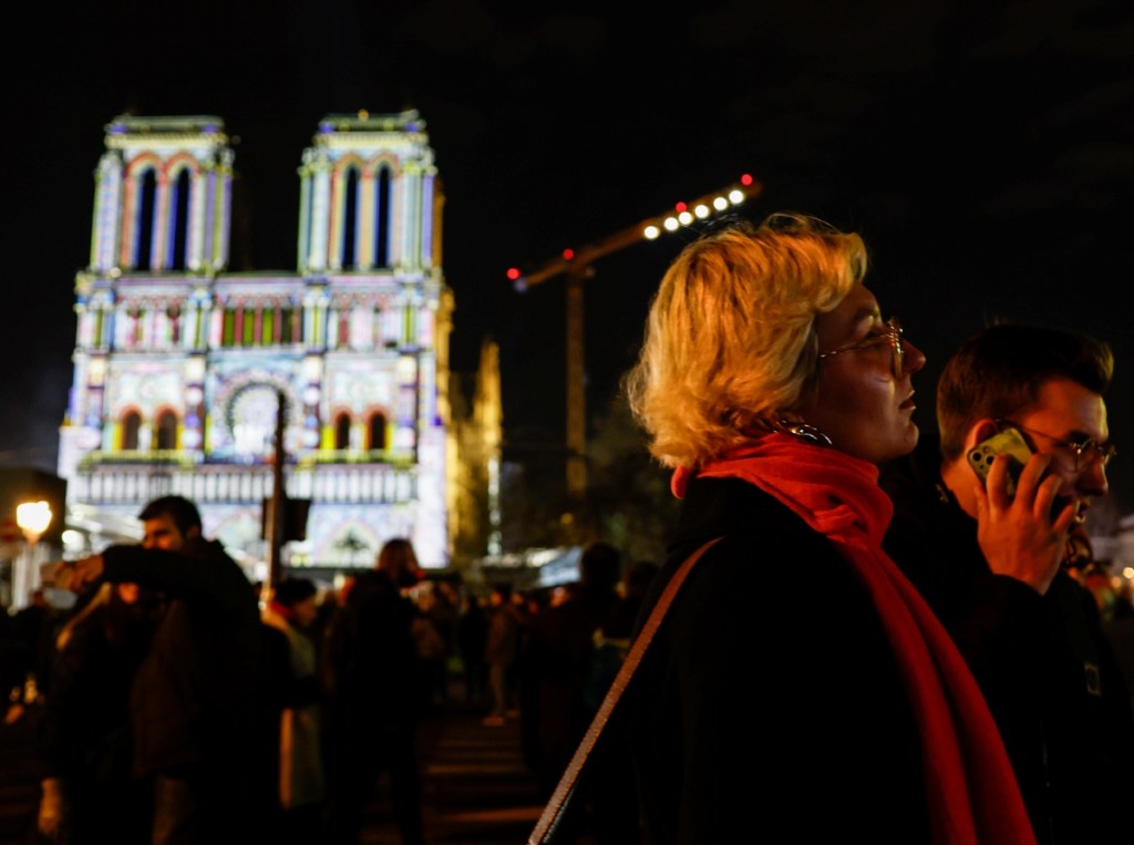 Peatones caminan frente a Notre Dame durante los preparativos finales para su reapertura esta noche en horario de París. A partir del lunes 16, la Catedral estará abierta al público desde las 7:45 hasta las 19 horas