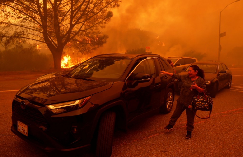 Una mujer se baja de su camioneta y rompe en llanto ante el avance de un incendio en el vecindario de Pacific Palisades, en las colinas de Los Ángeles, California, donde se emitieron órdenes de desalojo