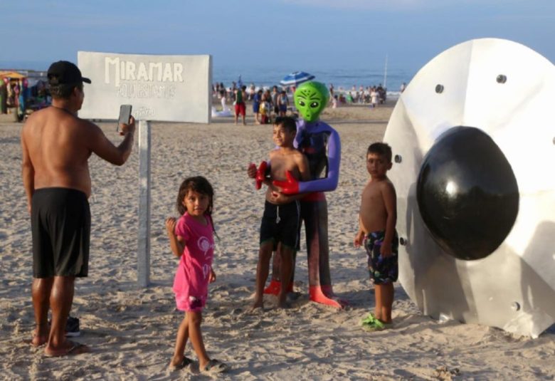 Turistas posan junto a una figura extraterrestre y una nave espacial en la playa Miramar, lugar conocido por su vínculo con el fenómeno ovni