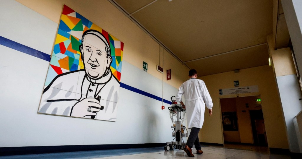 Un médico camina frente a un cuadro con la imagen del papa Francisco en un pasillo del Hospital Gemelli de Roma, donde se encuentra internado el Pontífice argentino