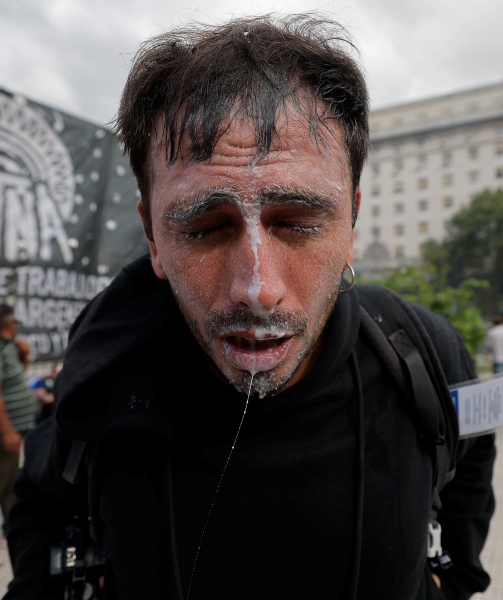 Una persona afectada con gas lacrimógeno intenta escapar del fragor del enfrentamiento. A la derecha, un detenido es sujetado por los policías