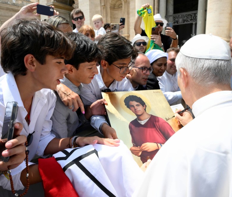 El papa León XIV firma a un grupo de jóvenes una imagen del beato italiano Carlo Acutis, conocido como “el santo milenial”, quien será canonizado el próximo 7 de septiembre, ayer en la plaza de San Pedro del Vaticano. A la derecha, el pontífice estadounidense saluda a la multitud congregada para escuchar su tradicional mensaje en la audiencia general de los miércoles