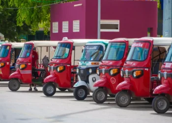 Varios mototaxis estacionados en fila frente a un edificio de color magenta.
