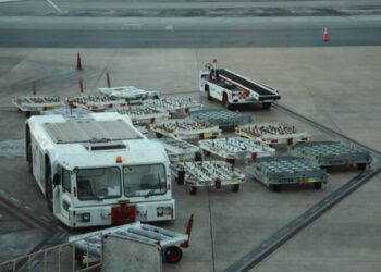 Carro de arrastre y varias plataformas de equipaje vacías sobre la pista de un aeropuerto.
