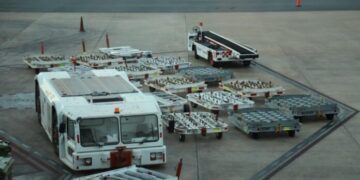 Carro de arrastre y varias plataformas de equipaje vacías sobre la pista de un aeropuerto.