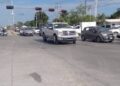 Cruce vial amplio con varios vehículos detenidos y semáforos en rojo bajo un cielo despejado.