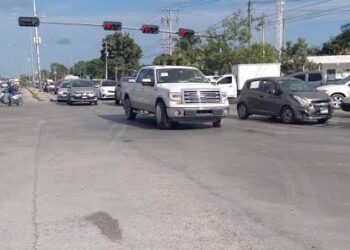 Cruce vial amplio con varios vehículos detenidos y semáforos en rojo bajo un cielo despejado.
